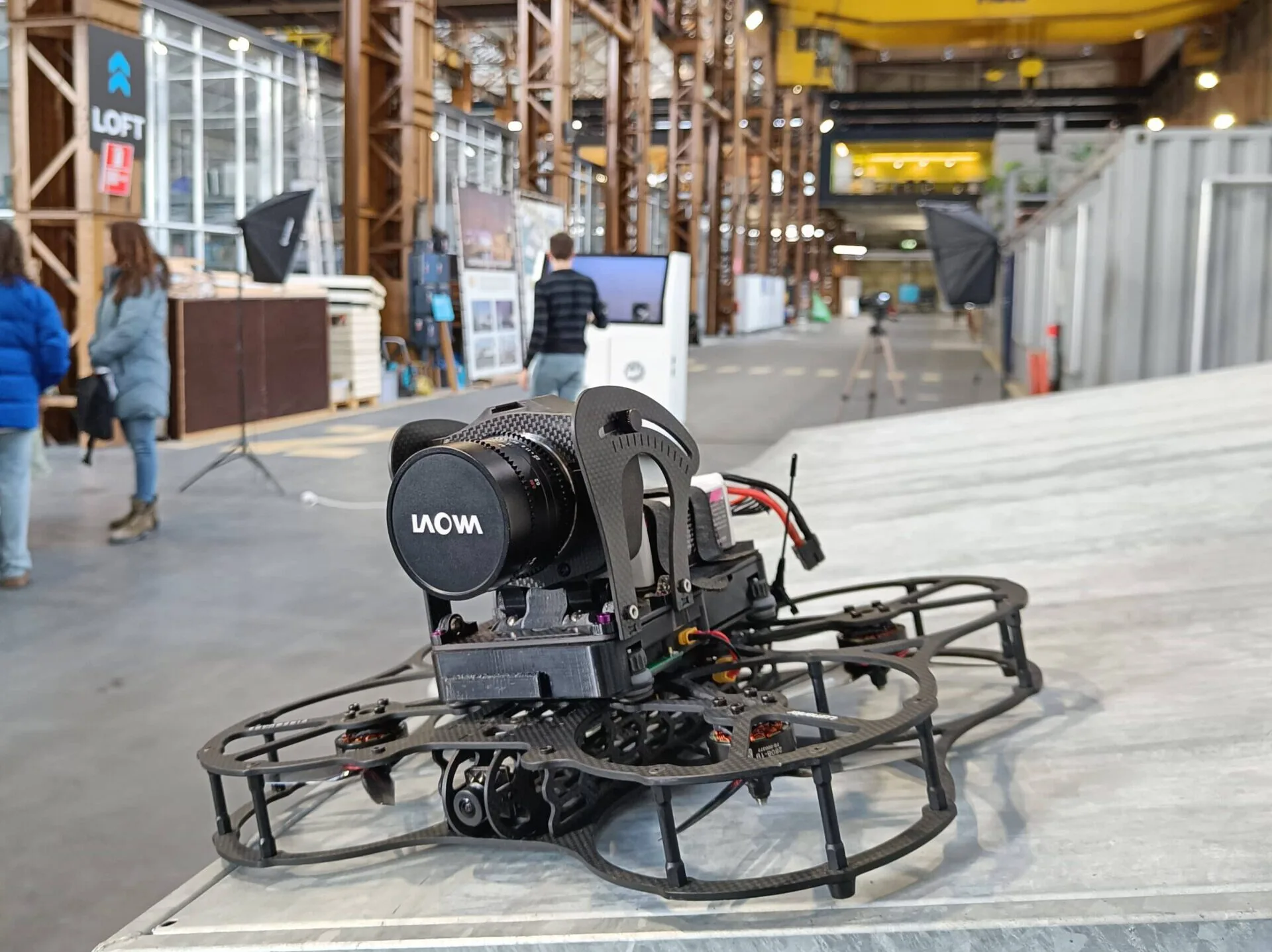 FPV-drone met camera in een grote industriële hal, met een studio-opstelling op de achtergrond