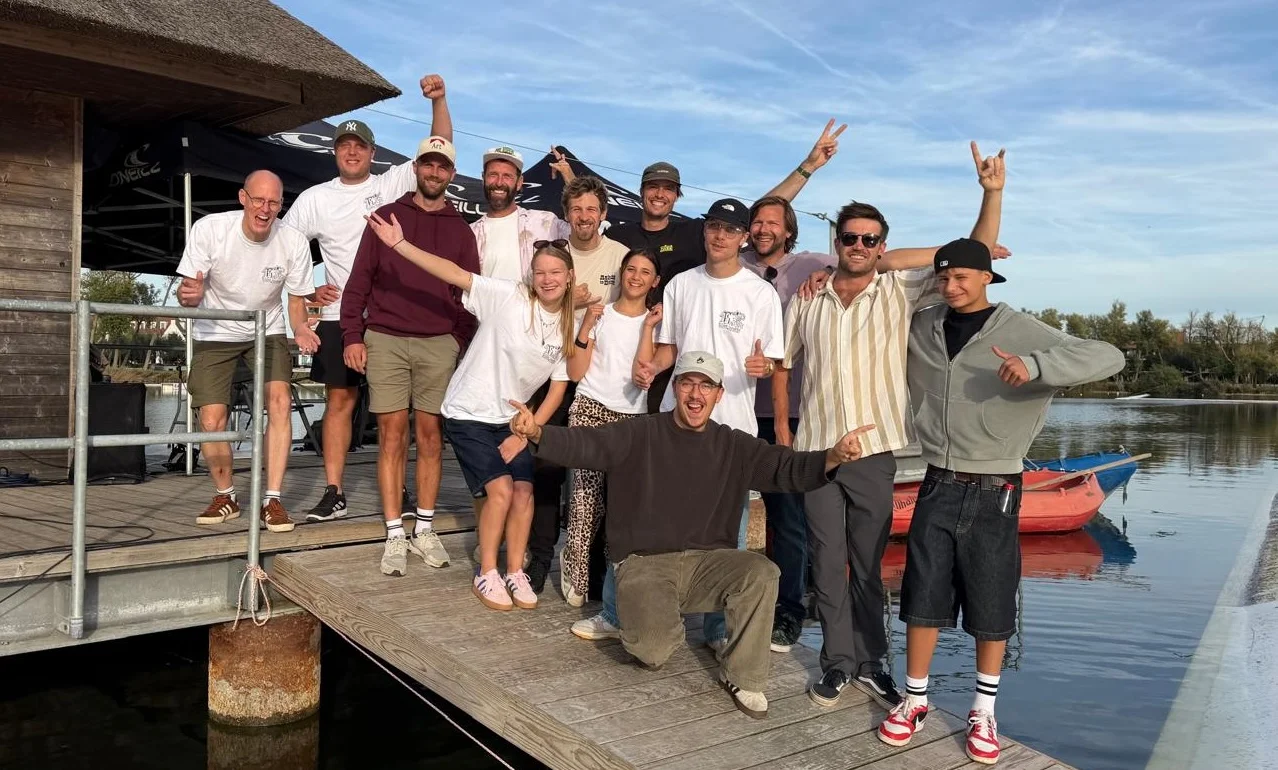 Het team op een steiger aan het water, met opgestoken armen en duimen